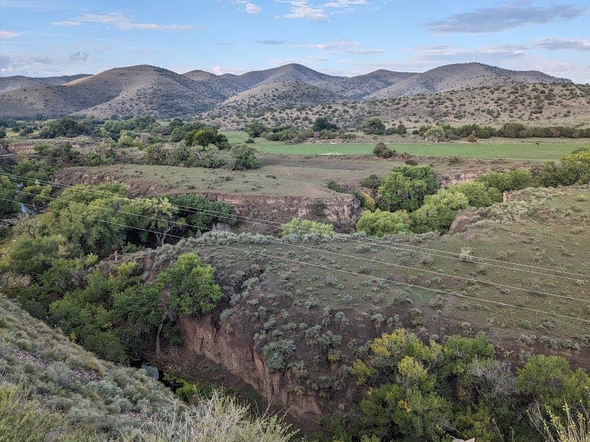 A green valley with a winding stream below dry, rolling hills
